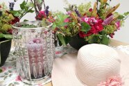 Bunte Blumenschale, Kerze im Glas und Strohhut in Pastell