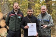 Drei Personen blicken in Kamera; eine hält eine Urkunde in der Hand